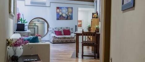 A hallway with wooden flooring leading to a living area with a sofa and a dining table.