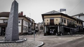 A cobblestone plaza with a prominent stone monument, a café with outdoor seating, and a building with a sign reading "Hostal Alpinista".