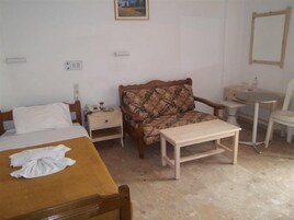 Habitación de hotel con cama, sofá, mesita, silla, mesita de noche, espejo y un cuadro colgado en la pared.