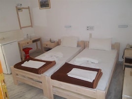Una habitación sencilla y limpia con dos camas individuales, un escritorio pequeño, una silla, un espejo y un taburete rojo.
