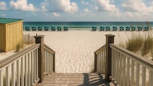Een houten looppad dat naar een strand leidt, met rijen groene parasols en ligstoelen.