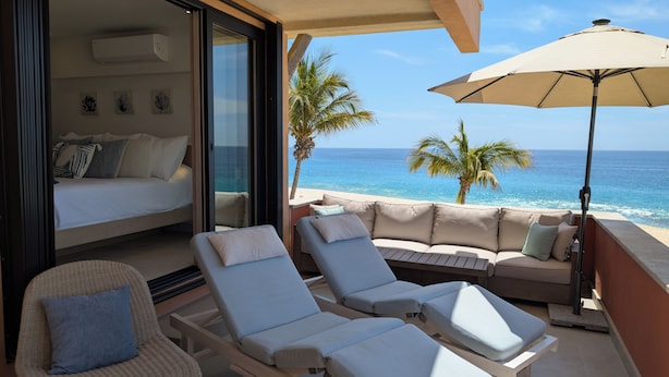 A balcony with a sofa, lounge chairs, and an umbrella overlooking the ocean.