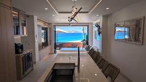 A modern kitchen with a view of the sea, a dining area with wicker chairs, and a ceiling fan.