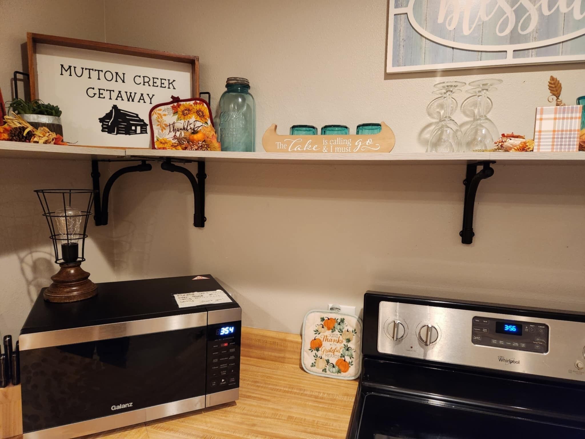 A kitchen with a microwave, a toaster, and a blender. There is a sign on the wall that reads "Mutton Creek Getaway".