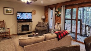 A cozy living room with a fireplace, a television, and a large window overlooking a wooded area. - Secluded Cabin Getaway with Firepit (Greenfield)
