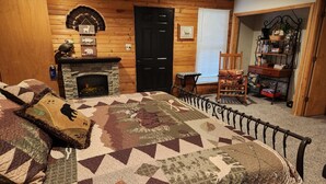 A cozy room with a large bed, a fireplace, a wooden wall, and a bookshelf. - Secluded Cabin Getaway with Firepit (Greenfield)
