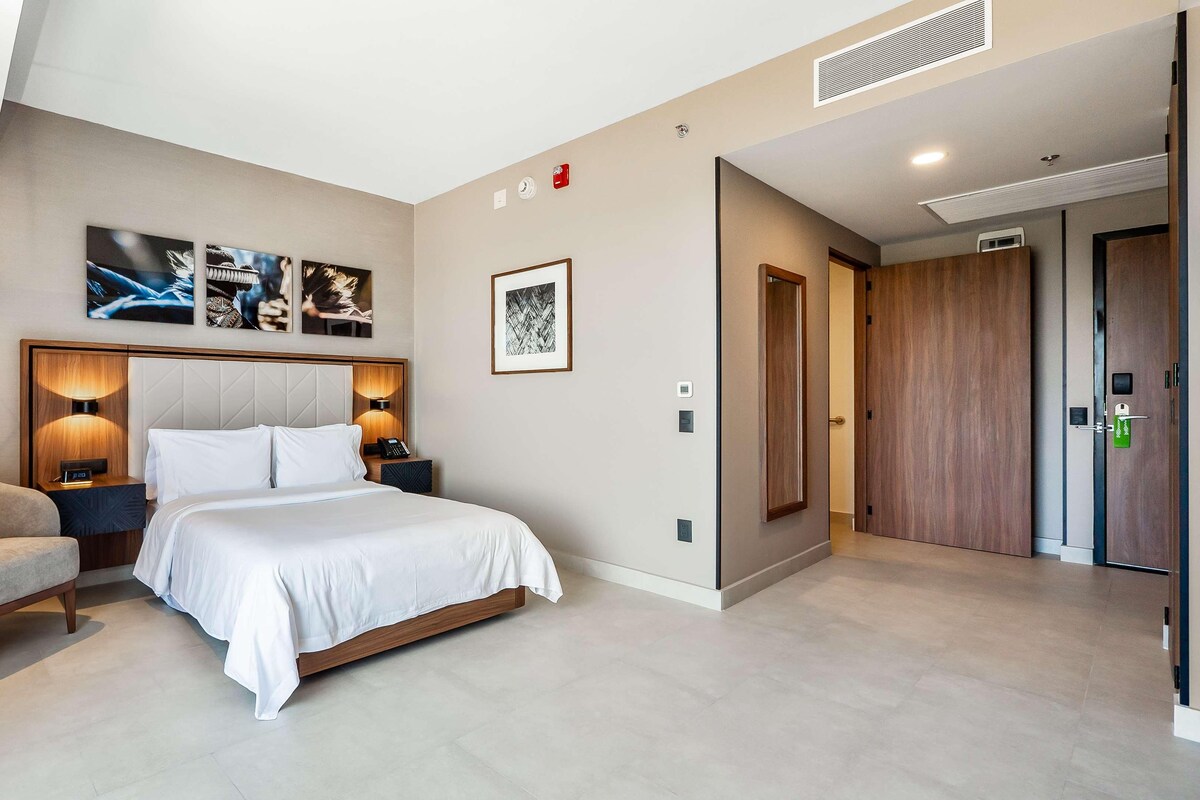 Una habitación de hotel moderna con una cama grande, una silla y obras de arte en las paredes.