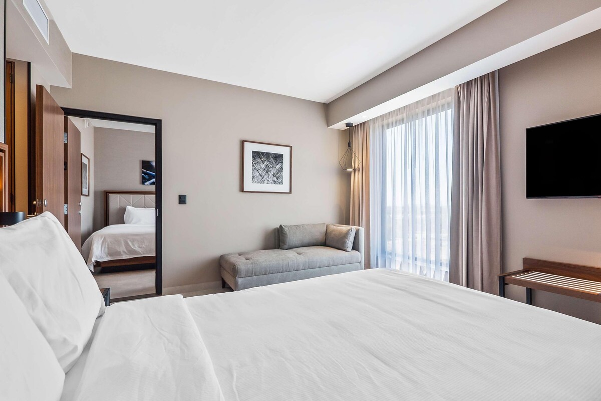 A hotel room with a large bed, a sofa, a desk, and a TV.