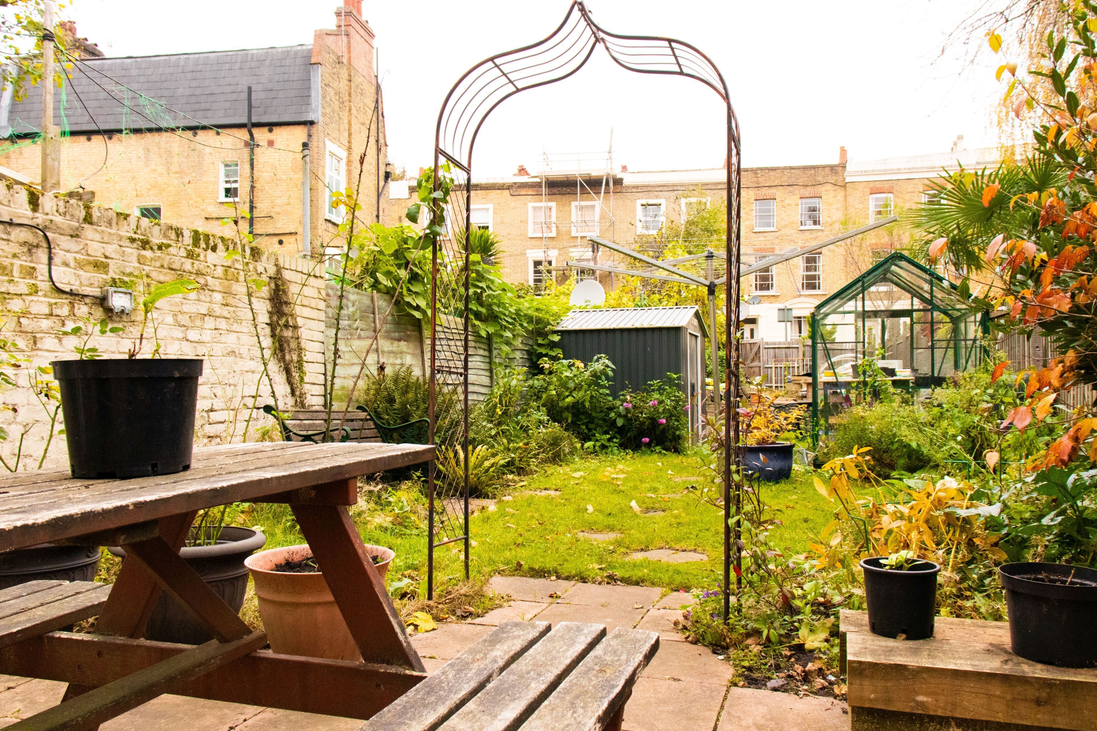 Een tuin met een houten bankje, planten in potten en een metalen boog.