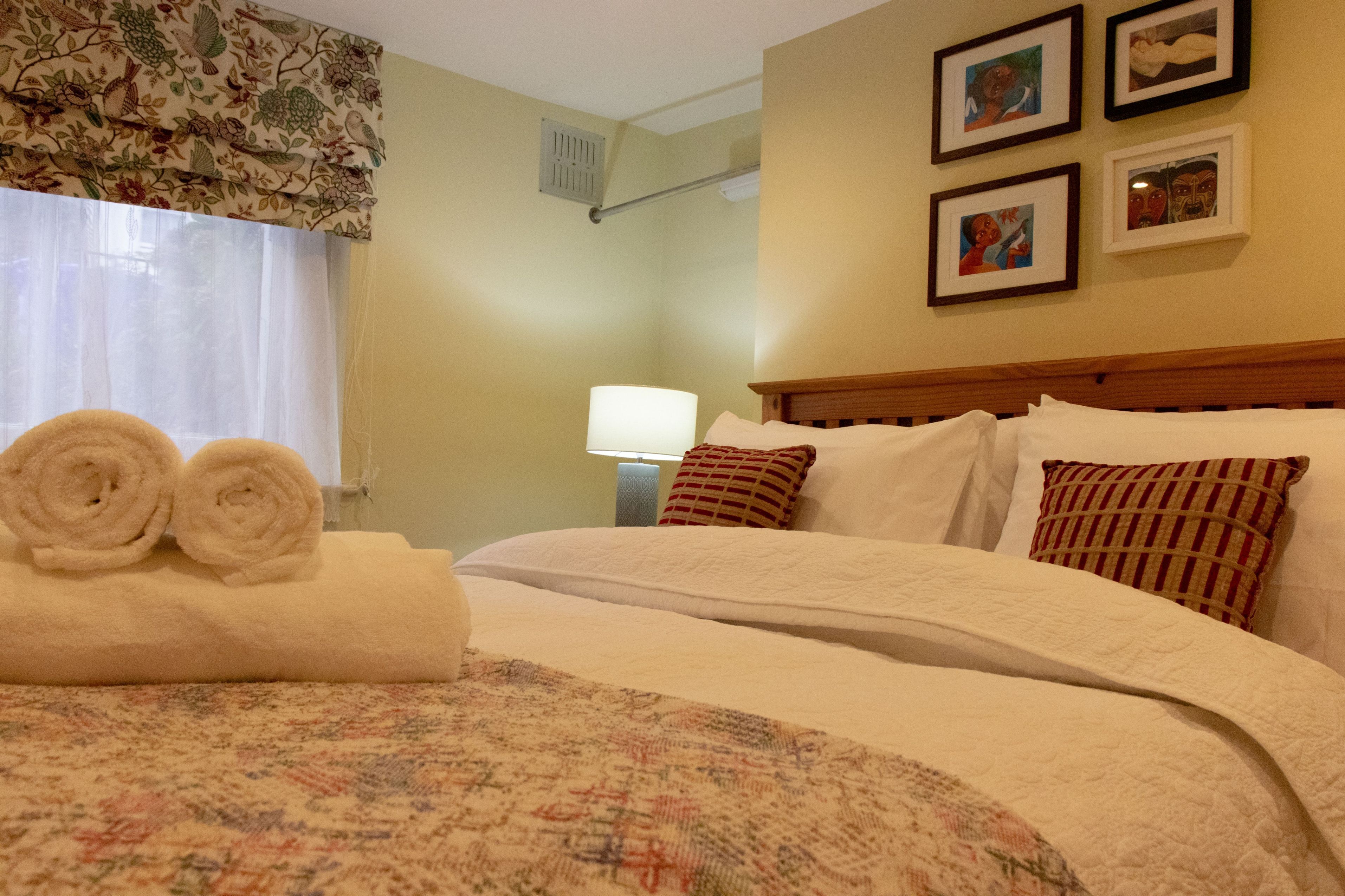Ein Hotelzimmer mit einem ordentlich bezogenen Bett, einer gemusterten Tagesdecke und einem Fenster mit floralen Vorhängen.