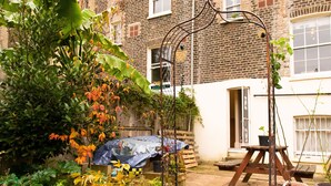 Un jardin avec une table en bois, une treille en métal et des plantes en pot.