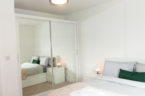 Quarto com cama, mesas de cabeceira, espelho e guarda-roupa.