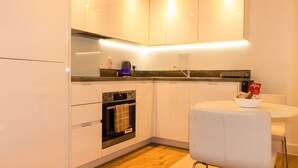 A modern kitchen with white cabinets, a built-in oven, a coffee maker, and a small dining table with a bowl of snacks. - Livestay - 1bed Apt Private Building Free Parking (Luton)