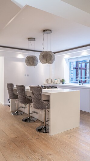 A modern kitchen with a central island, three bar stools, pendant lights, and a window with a view. - Exquisite 2400sqft 3 Bed Brick Lane Pad (London)