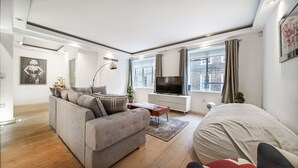 Ett modernt vardagsrum med en grå soffa, en platt-TV och ett stort fönster med gardiner.