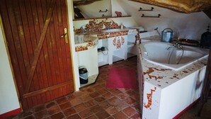 Een rustieke badkamer met een houten deur, betegelde vloer, een wastafel en een bad.
