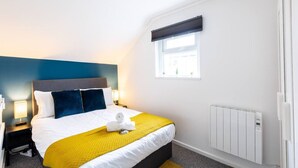 A hotel room with a bed, nightstands, a window, and a radiator. - Dan Suite by Koya Homes (Barry)