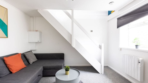 A modern living room with a grey sofa, a small round table, and a staircase. - Dan Suite by Koya Homes (Barry)