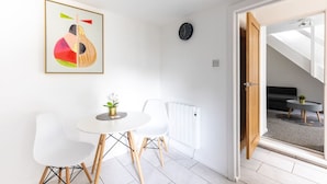 A modern, well-lit room with a dining table and chairs, a radiator, a clock, and a door leading to a staircase. - Dan Suite by Koya Homes (Barry)