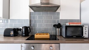 A modern kitchen with a stainless steel range hood, a toaster, a coffee maker, a microwave, and a wooden spice rack. - Dan Suite by Koya Homes (Barry)