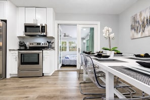 A modern kitchen with stainless steel appliances, a dining area with a white table and chairs, and a view into a bedroom with a bed and a window. - Pool Home, Sleeps 8, Hollywood Beach | Near Hard Rock, Monthly Stays Welcome (Hollywood)