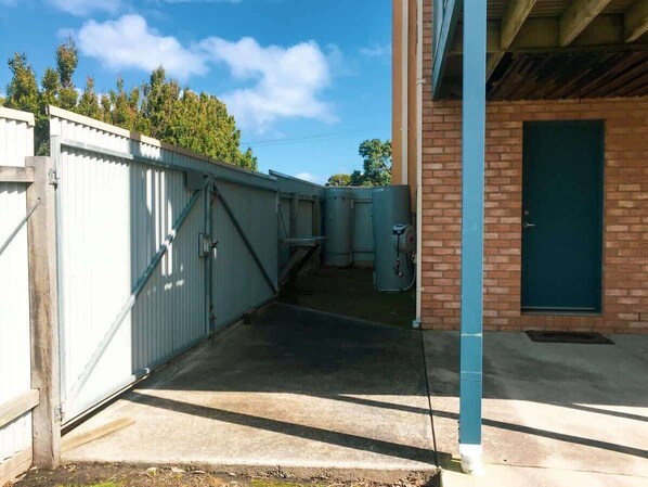 Un área industrial resguardada por una cerca metálica, con suelo de concreto y un edificio de ladrillo con una puerta verde.
