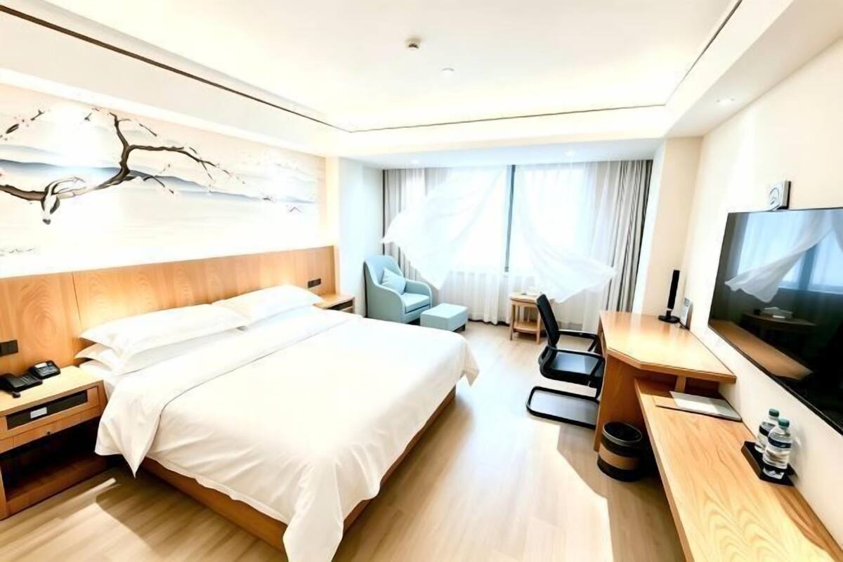 Quarto de hotel com cama, escrivaninha, cadeira, televisão e janela com cortinas.