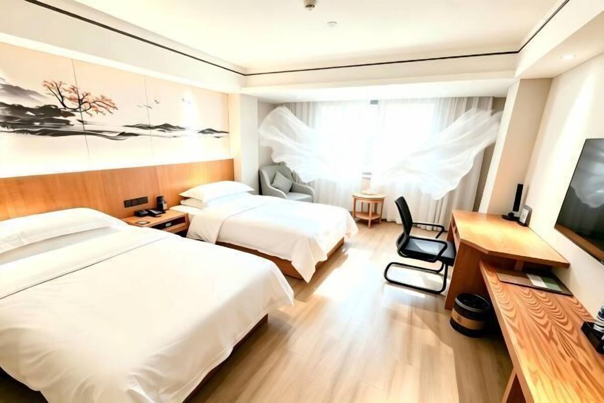 Quarto de hotel com duas camas, uma escrivaninha, uma cadeira e uma televisão.