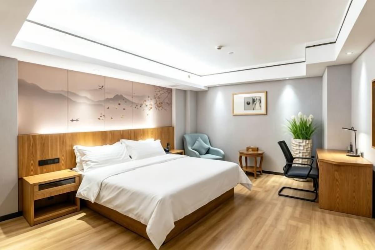 Quarto de hotel moderno com uma cama grande, uma escrivaninha, uma cadeira e uma mesinha.