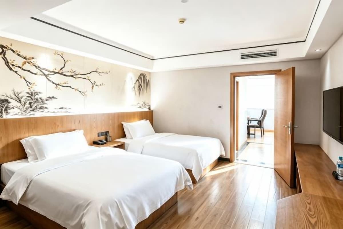 Quarto de hotel com duas camas, televisão e piso de madeira.