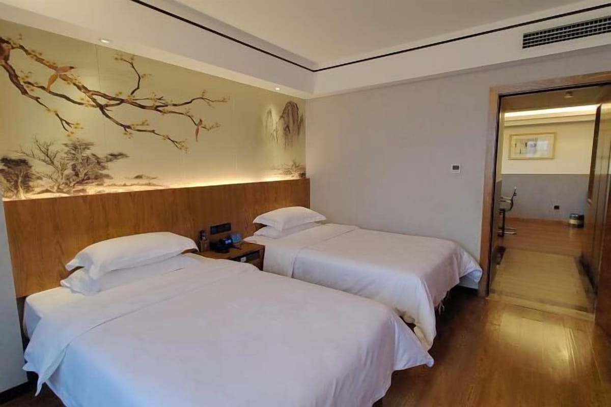 Hotellihuone, jossa on kaksi sänkyä, puinen pääty, seinämaalaus ja puulattia.