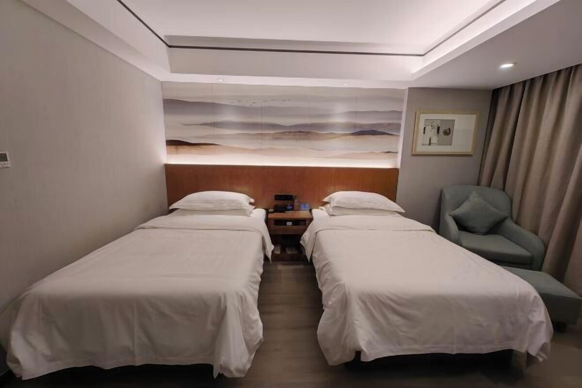 Ein Hotelzimmer mit zwei Betten, einem Schreibtisch, einem Sessel und einem Bild an der Wand, mit Blick ins Freie.