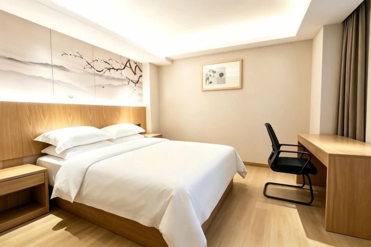 Quarto de hotel com cama, mesa de cabeceira, escrivaninha e cadeira.