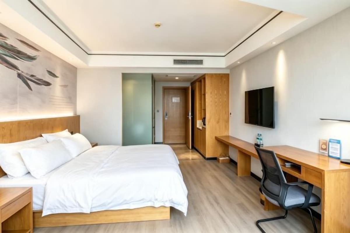Quarto de hotel com cama, escrivaninha, cadeira, televisão e um quadro na parede.