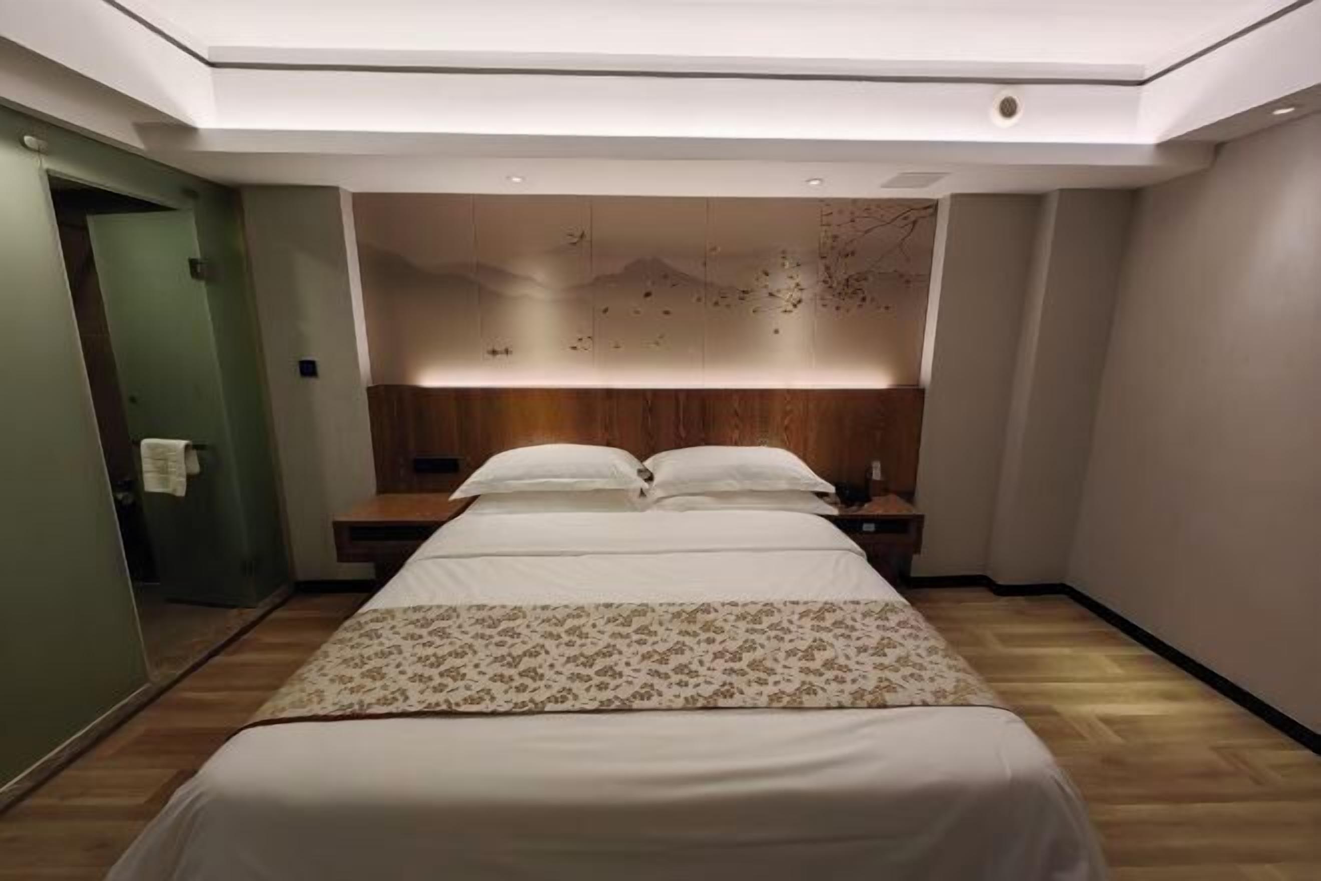 A modern hotel room with a large bed, wooden headboard, and a decorative wall panel.