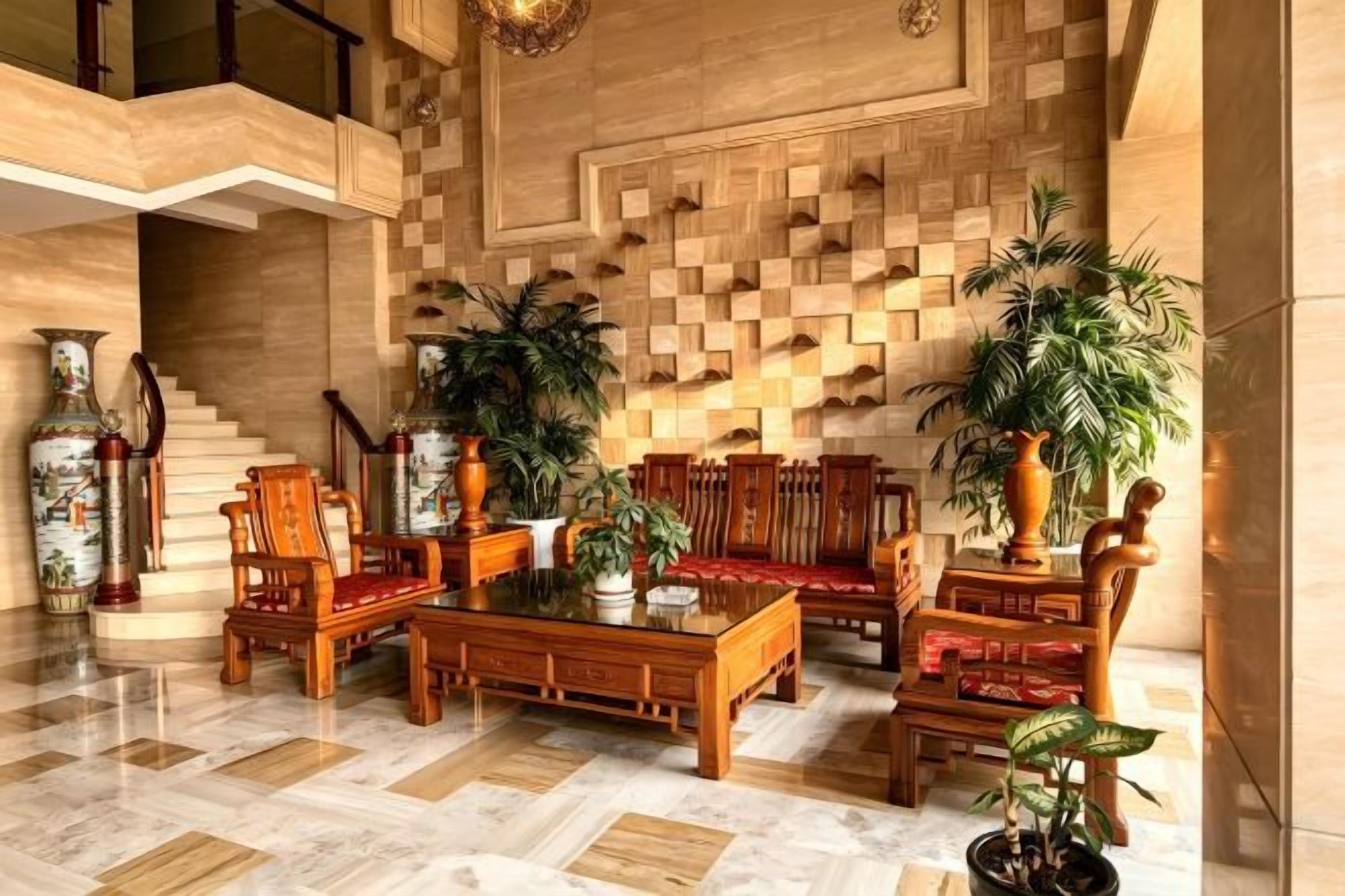 A lobby with a wooden floor, a central seating area with chairs and a table, and a staircase in the background.