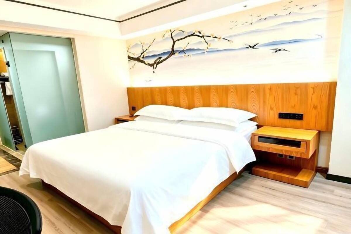 Quarto de hotel com cama, cabeceira de madeira, mesa de cabeceira e uma obra de arte na parede.