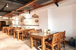 A dining area with wooden tables and chairs, pendant lighting, and a wall with artwork.