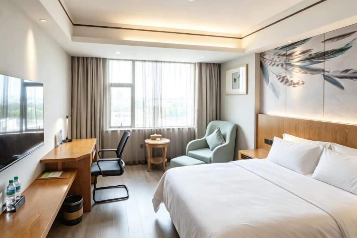 Quarto de hotel com cama, escrivaninha, cadeira, mesa pequena e televisão.