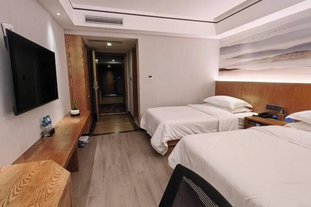 Quarto de hotel com duas camas, uma televisão, uma escrivaninha e parede revestida de madeira.
