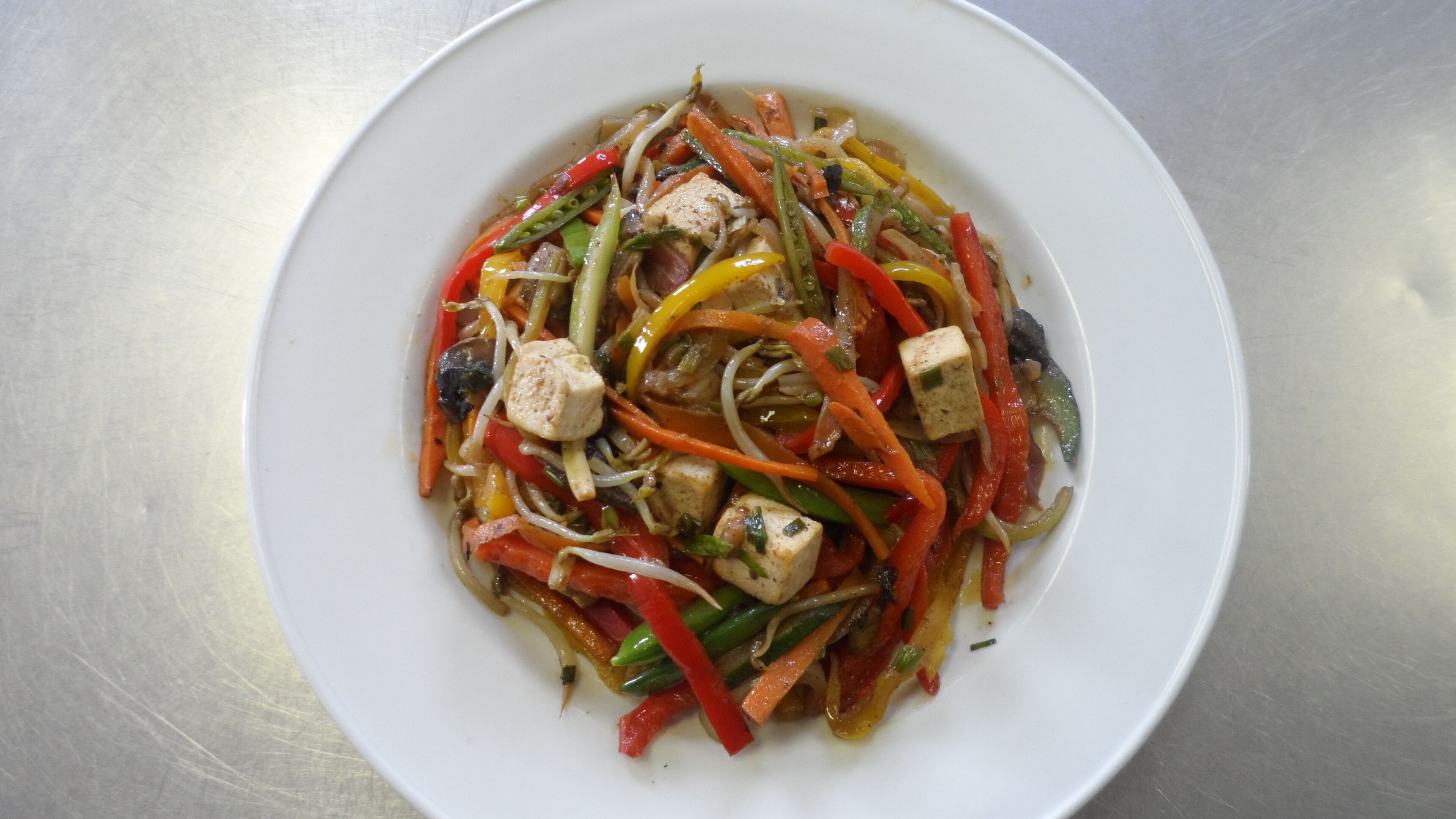 Un plato blanco con un salteado de verduras y tofu.