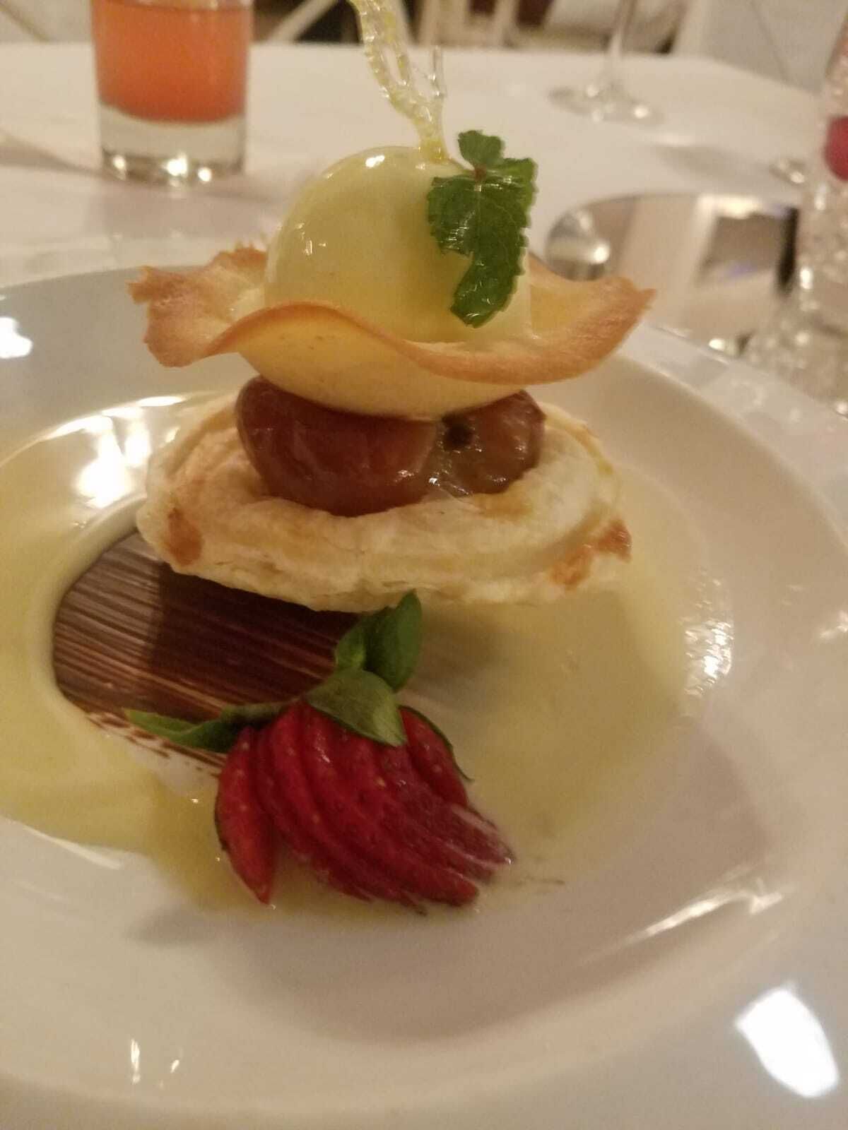 A dessert plate with a layered pastry, a strawberry, and a mint leaf garnish.
