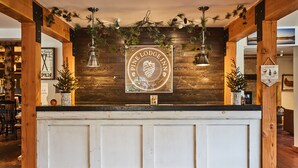 Ein Empfangstresen mit dem Logo des Pine Lodge Inn, Holzbalken und hängenden Lampen.