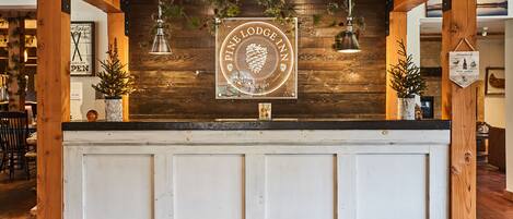 Una recepción con el logotipo de Pine Lodge Inn, vigas de madera y luces colgantes.