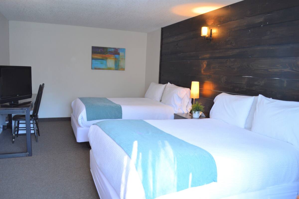 A hotel room with two beds, a desk with a chair, a television, and a painting on the wall.