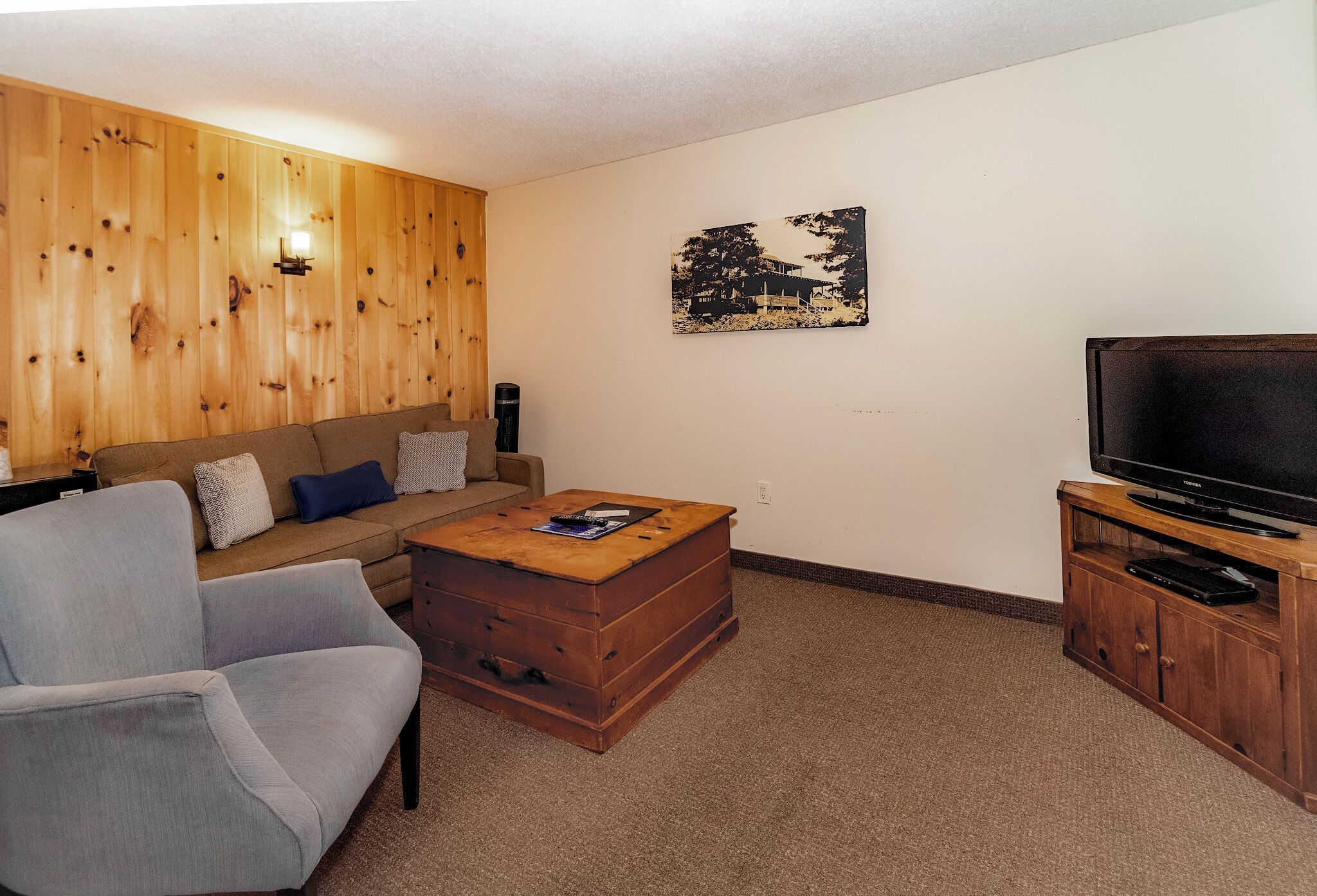 Een woonkamer met een houten wand, een bank, een salontafel, een televisie en een kast.