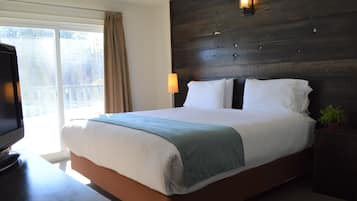 A hotel room with a large bed, a TV on a desk, a window with curtains, and a wooden headboard with wall-mounted lights.