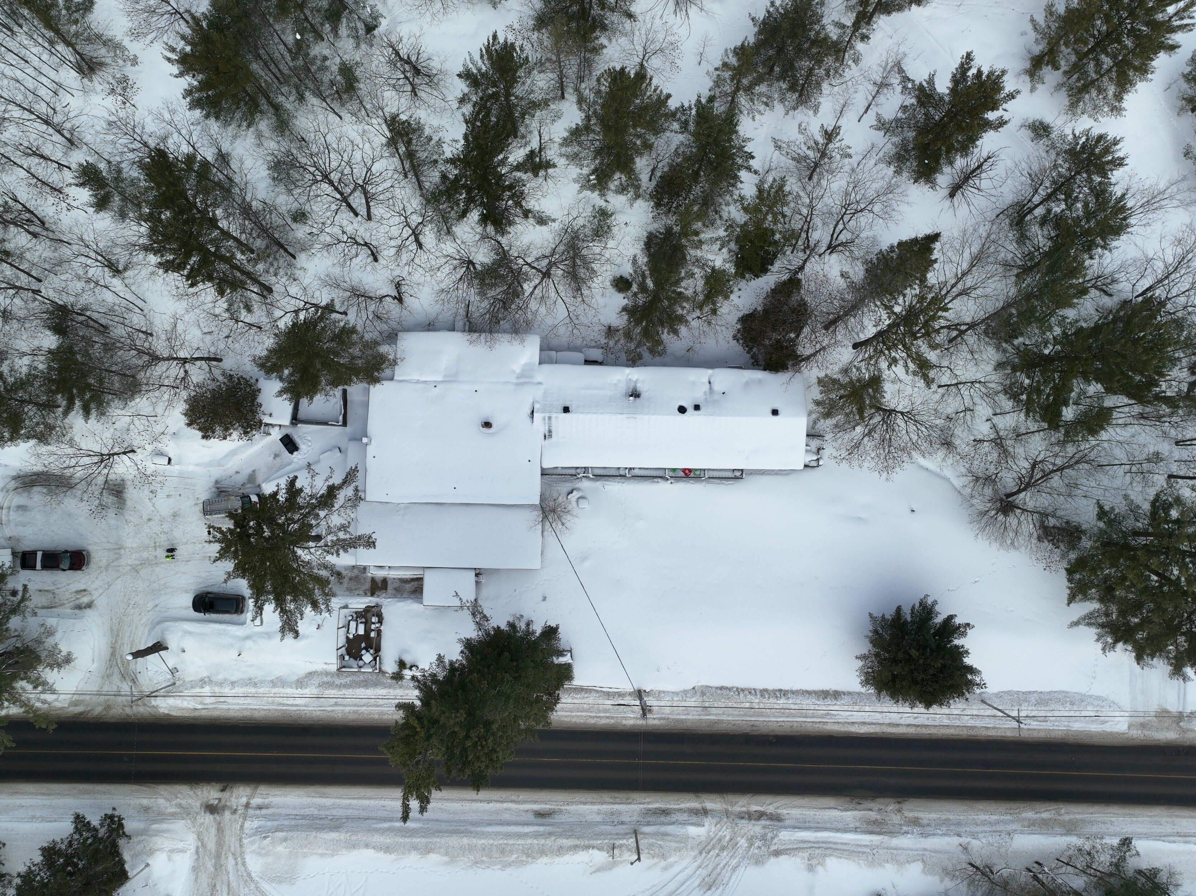 A snow-covered building with a flat roof, surrounded by trees and a road.