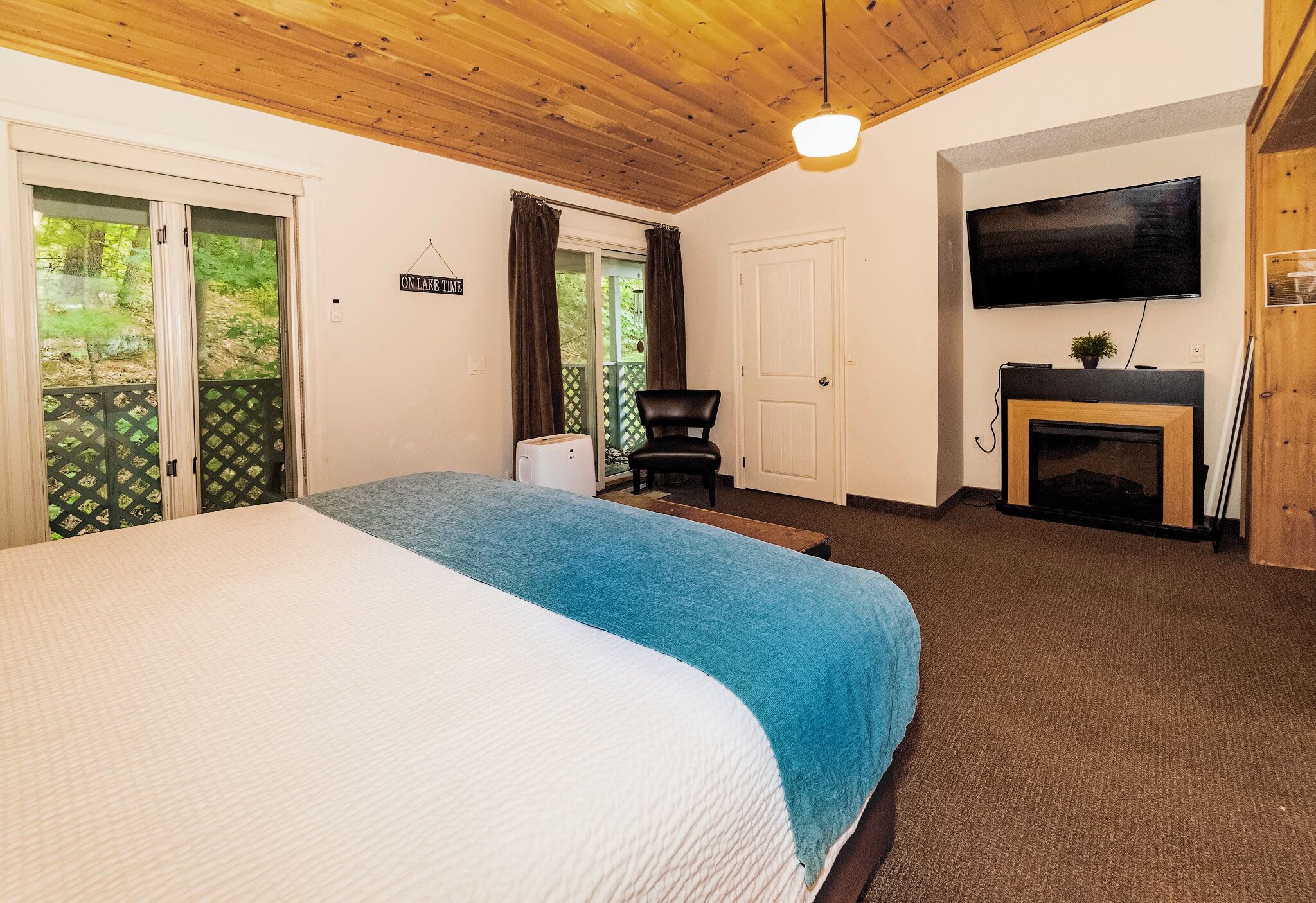 A bedroom with a bed, a television, a fireplace, and a sliding door to a balcony.