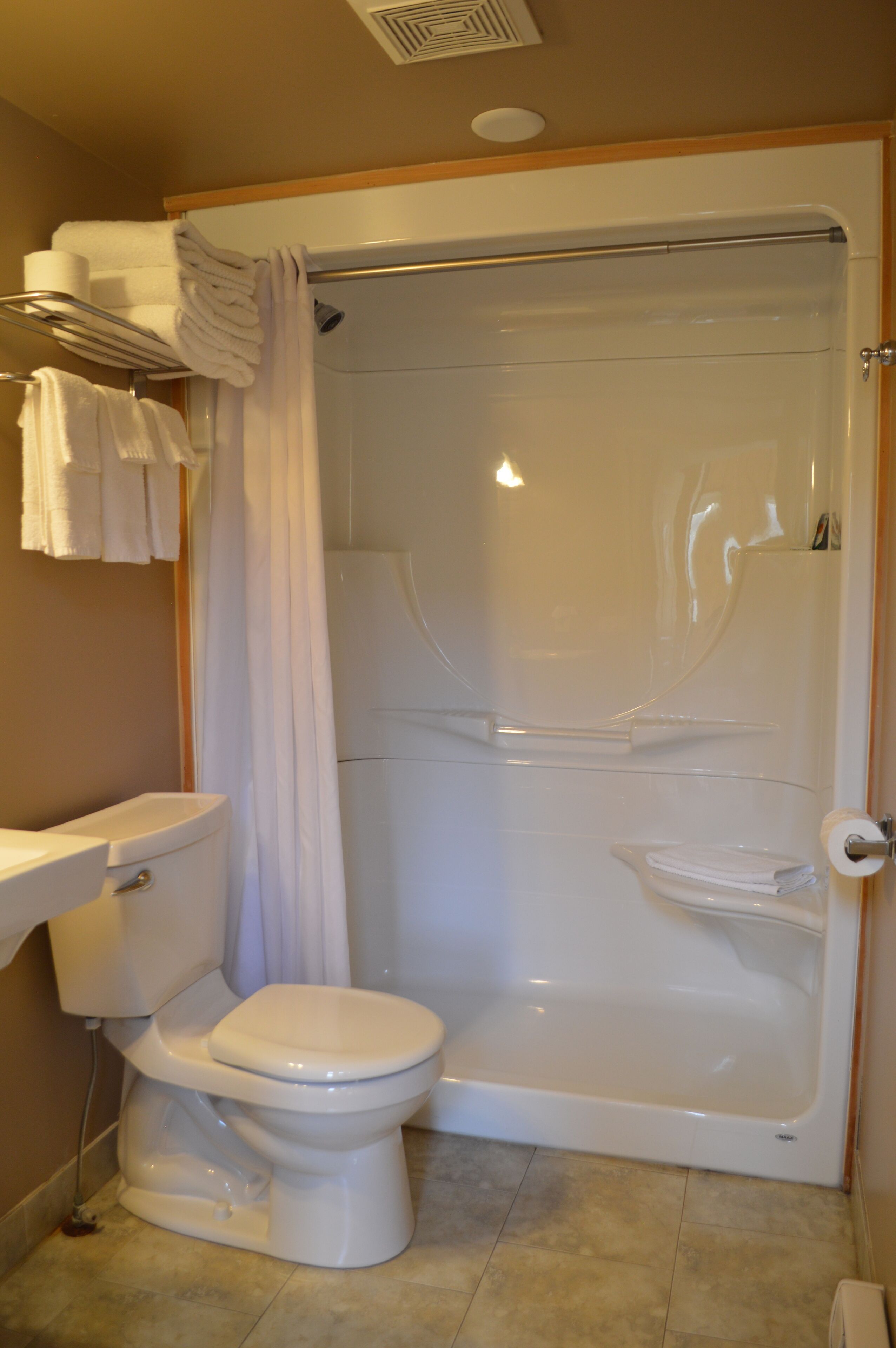 Un baño con cabina de ducha, inodoro y un perchero con toallas dobladas.